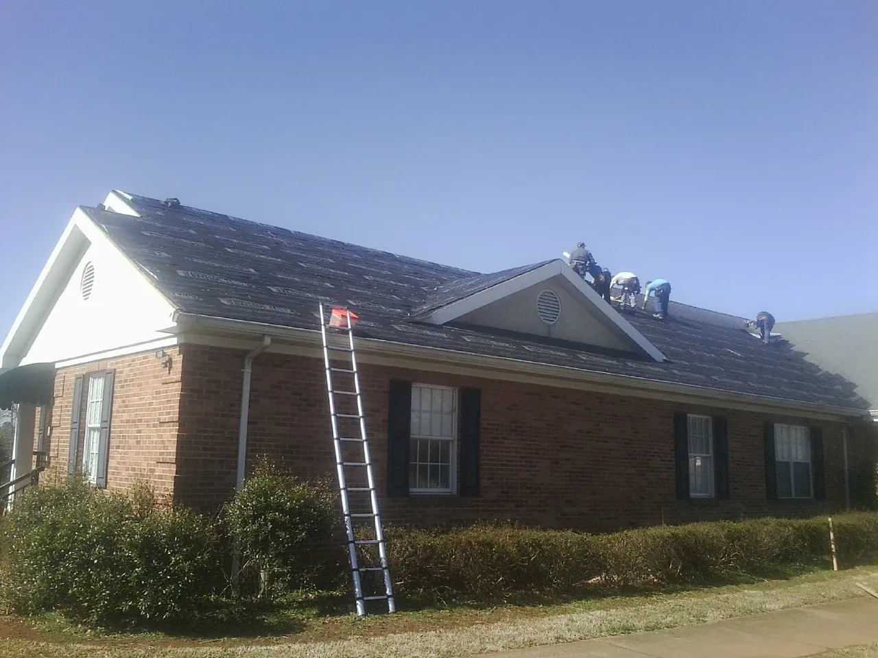 Crew tearing shingles off a brick ranch roof with a ladder set — Metal Roof Repair work by our crew in Irwin